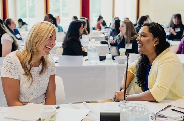 Two women laughing at a table during a conference.