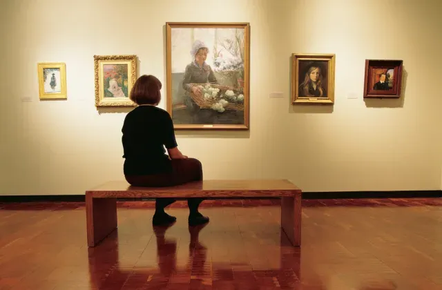 博物馆的参观者坐在长凳上欣赏一幅女孩的画