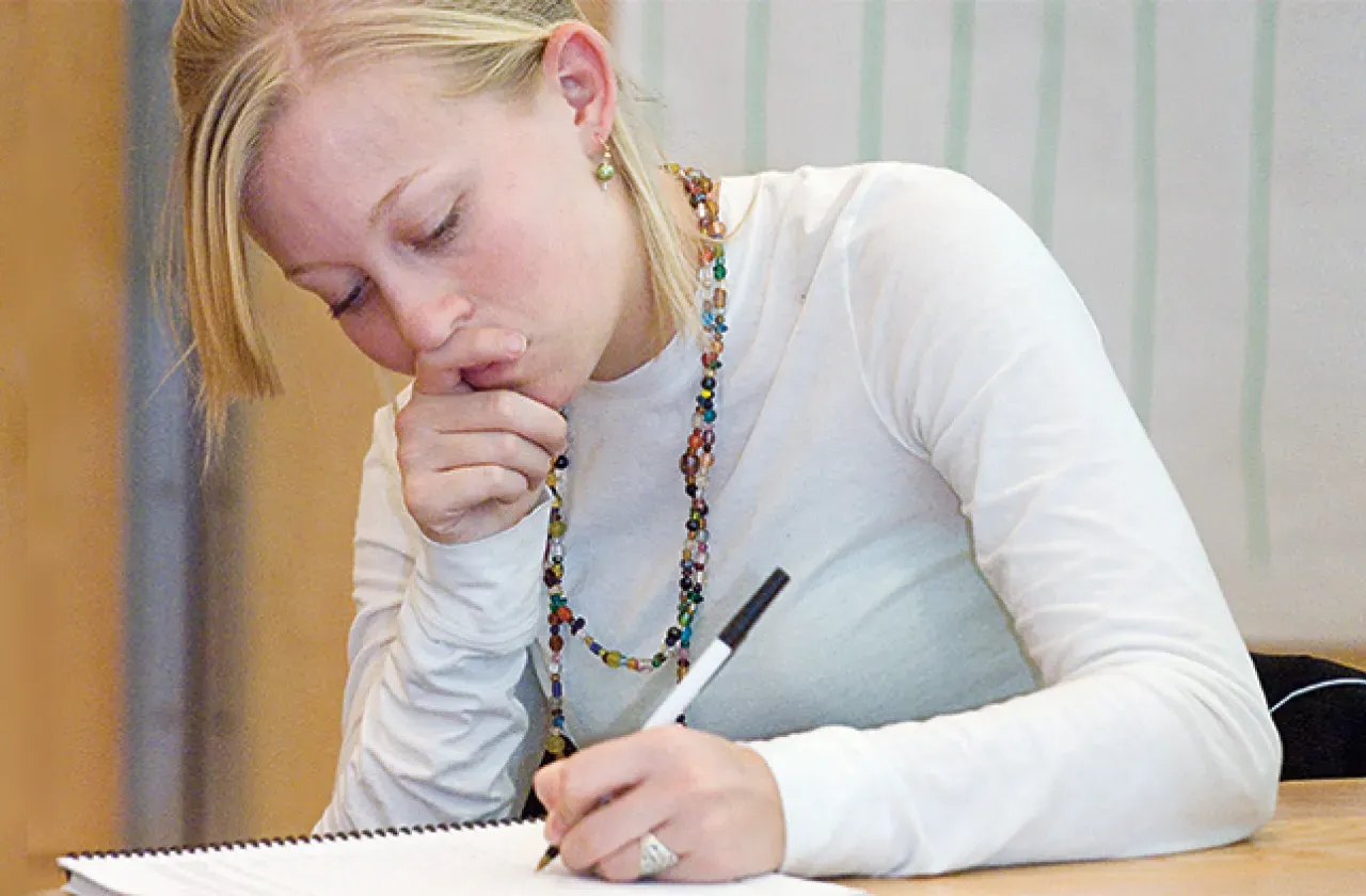 Student in white sweater writing in a notebook