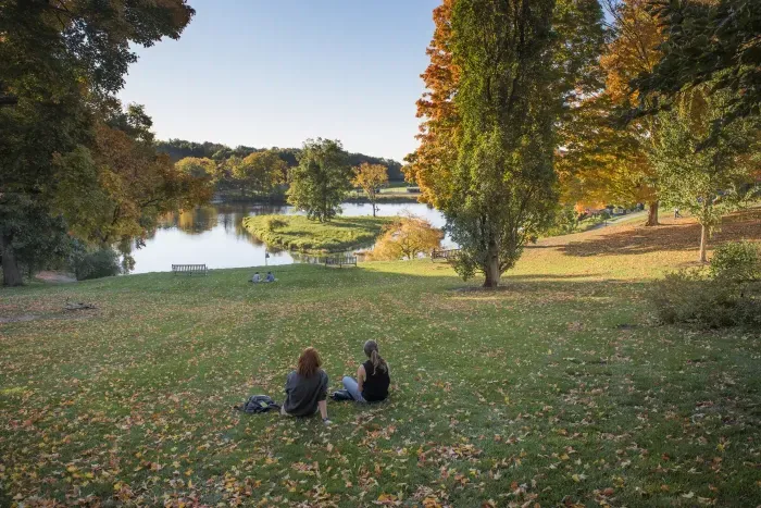 Two students sitting in front of Paradise Pond in the fall.