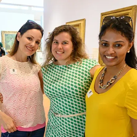 Three alumnae standing close together and smiling in the Smith College Museum of Art